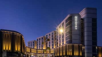 Un hotel moderno con un llamativo letrero de 'NOVOTEL', que presenta una fachada curva y una entrada bien iluminada.