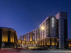 Un hotel moderno con un llamativo letrero de 'NOVOTEL', que presenta una fachada curva y una entrada bien iluminada.