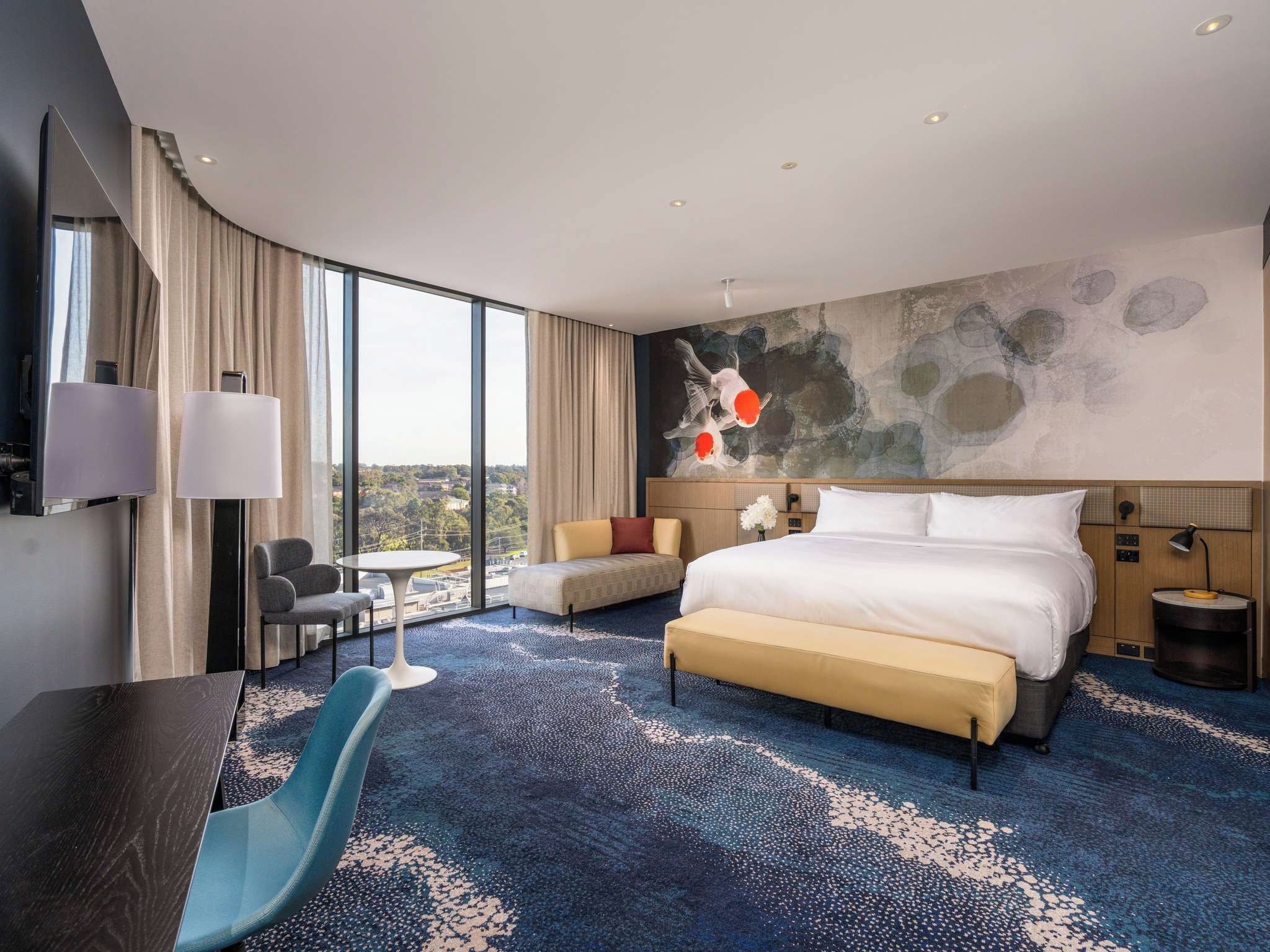 Une chambre d’hôtel moderne, dotée d’un grand lit, d’un bureau, d’une chaise, d’une petite table et offrant une vue sur la ville.