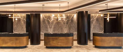 Un área de recepción con tres mostradores curvos, paredes de mármol e iluminación moderna.