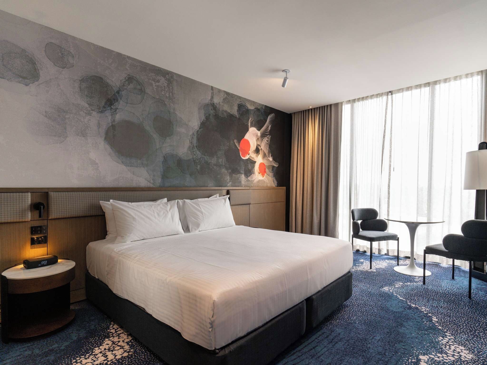 A hotel room with a large bed, a desk, a chair, and a wall with abstract art.