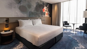 A hotel room with a large bed, a desk, a chair, and a wall with abstract art. - Novotel Sydney Cabramatta (Sydney)