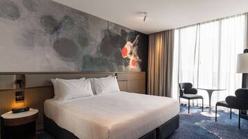 A hotel room with a large bed, a desk, a chair, and a wall with abstract art.