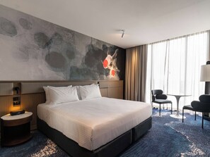 A hotel room with a large bed, a desk, a chair, and a wall with abstract art. - Novotel Sydney Cabramatta (Sydney)