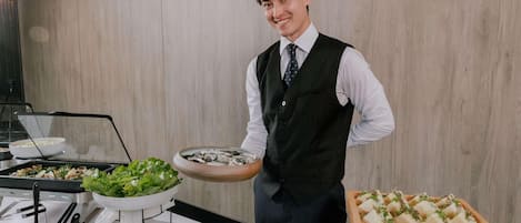 Una persona sirviendo comida en un bufé, con varios platos y utensilios a la vista.