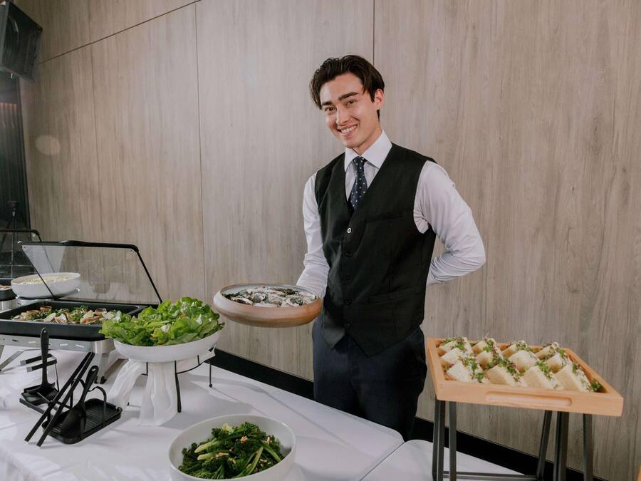 A person serving food at a buffet with various dishes and utensils visible.