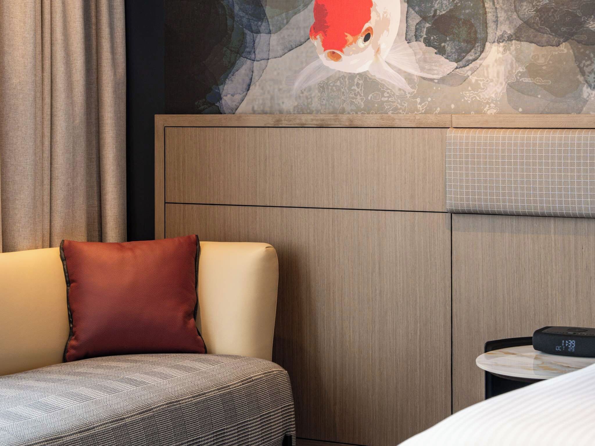 Quarto de hotel com cama, sofá, relógio digital e pintura de carpa.