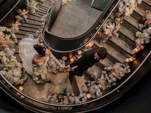 A wedding ceremony on a curved staircase with floral arrangements and candles.
