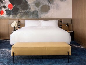 A hotel room with a large bed, a bench, a nightstand with a lamp, and a wall with a fish mural.
