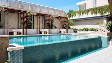 A swimming pool with a tiled edge, stone walls, and a pergola structure.
