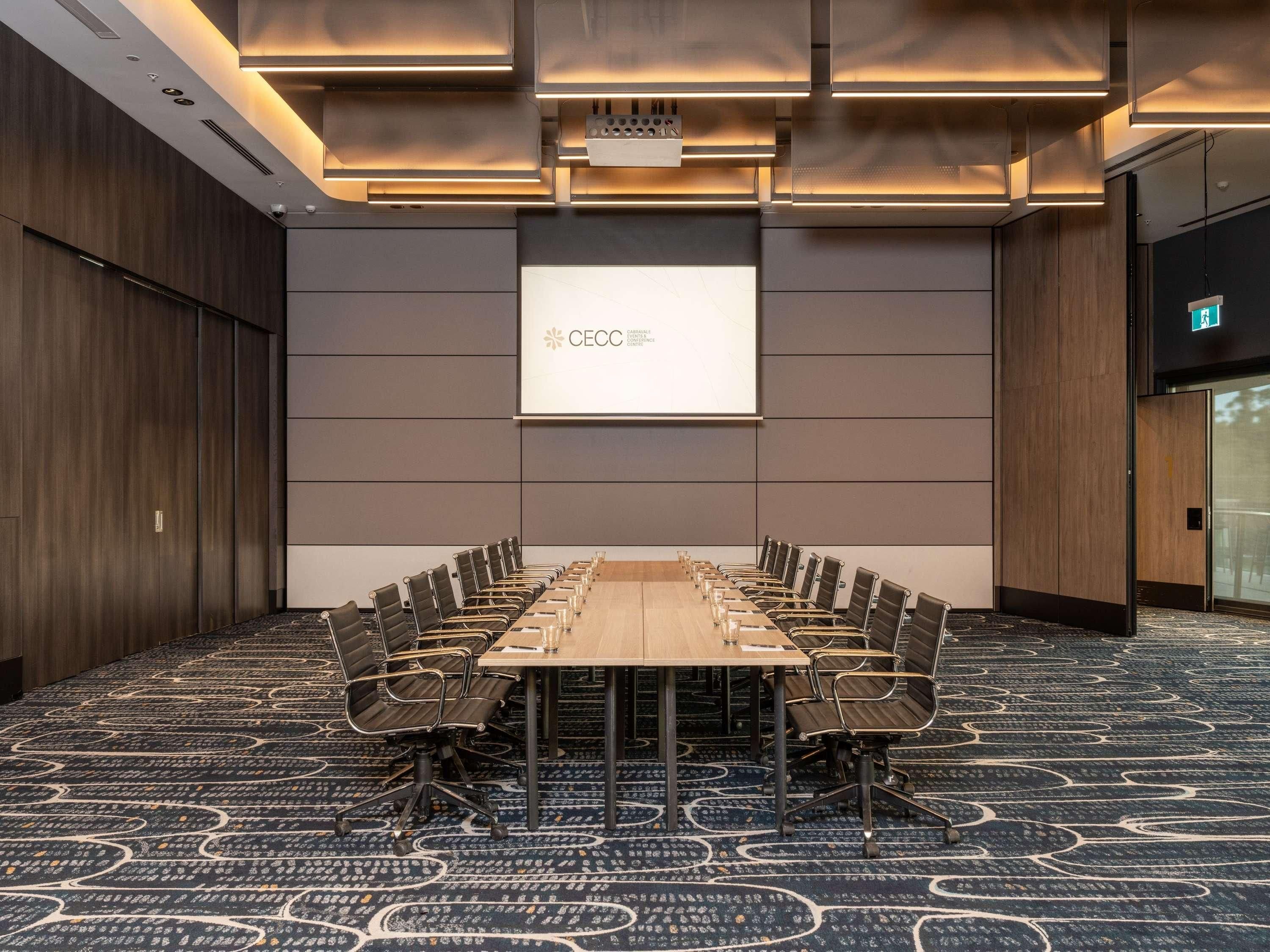 A conference room with a long table, chairs, a projector screen, and a carpeted floor.