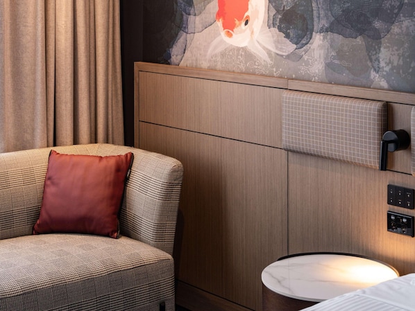A hotel room with a houndstooth sofa, a red pillow, a marble side table, a painting on the wall, and a wooden paneling design. - Novotel Sydney Cabramatta (Sydney)