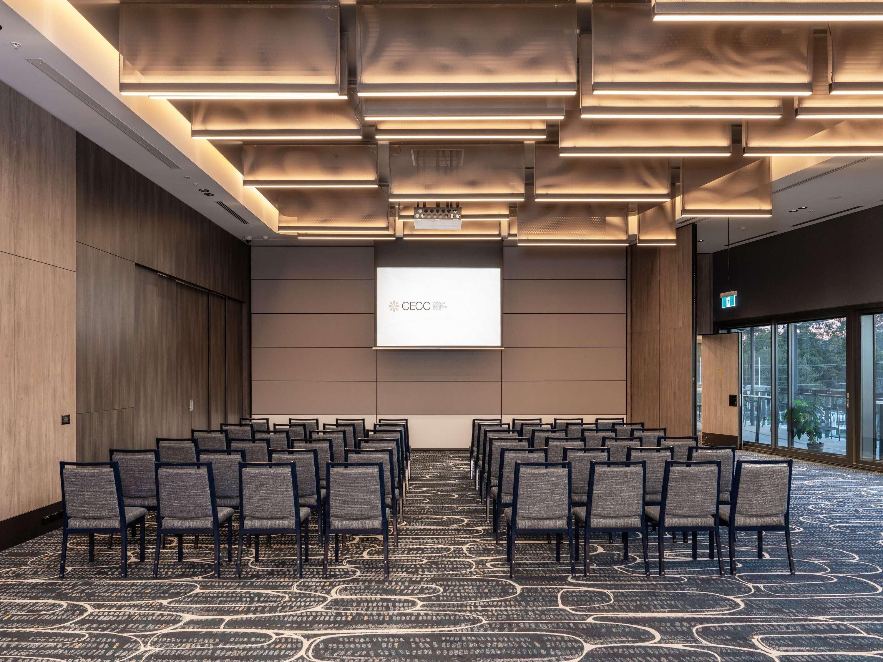 A conference room with rows of chairs, a projector screen, and a large window.