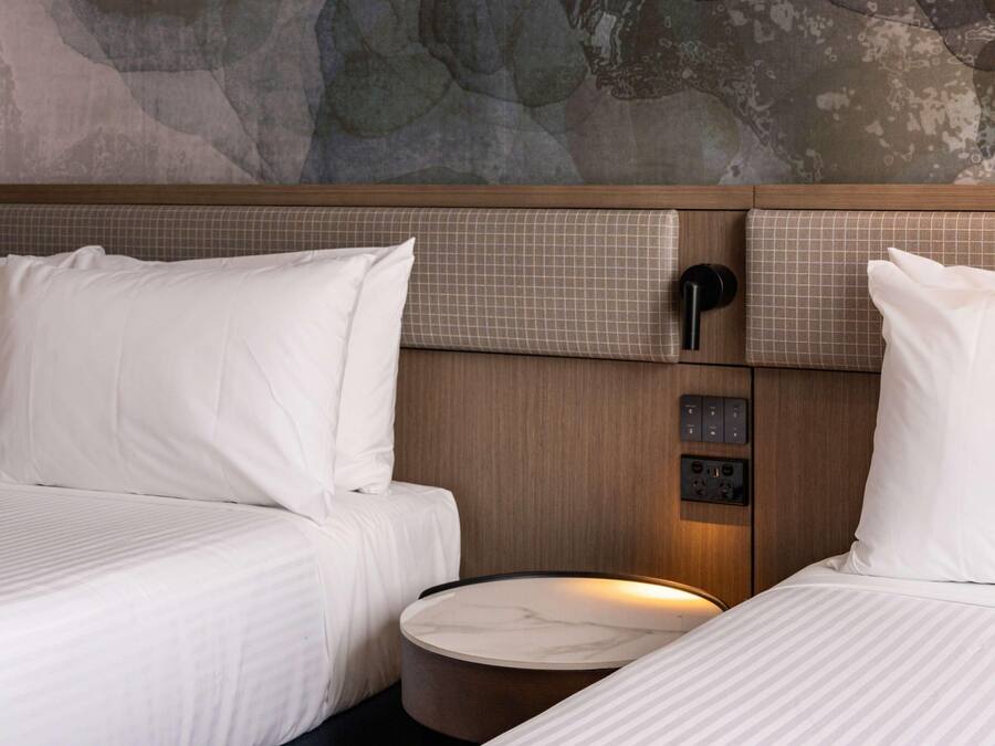 Habitación de hotel con dos camas, un panel de control y una mesa de tocador de mármol.