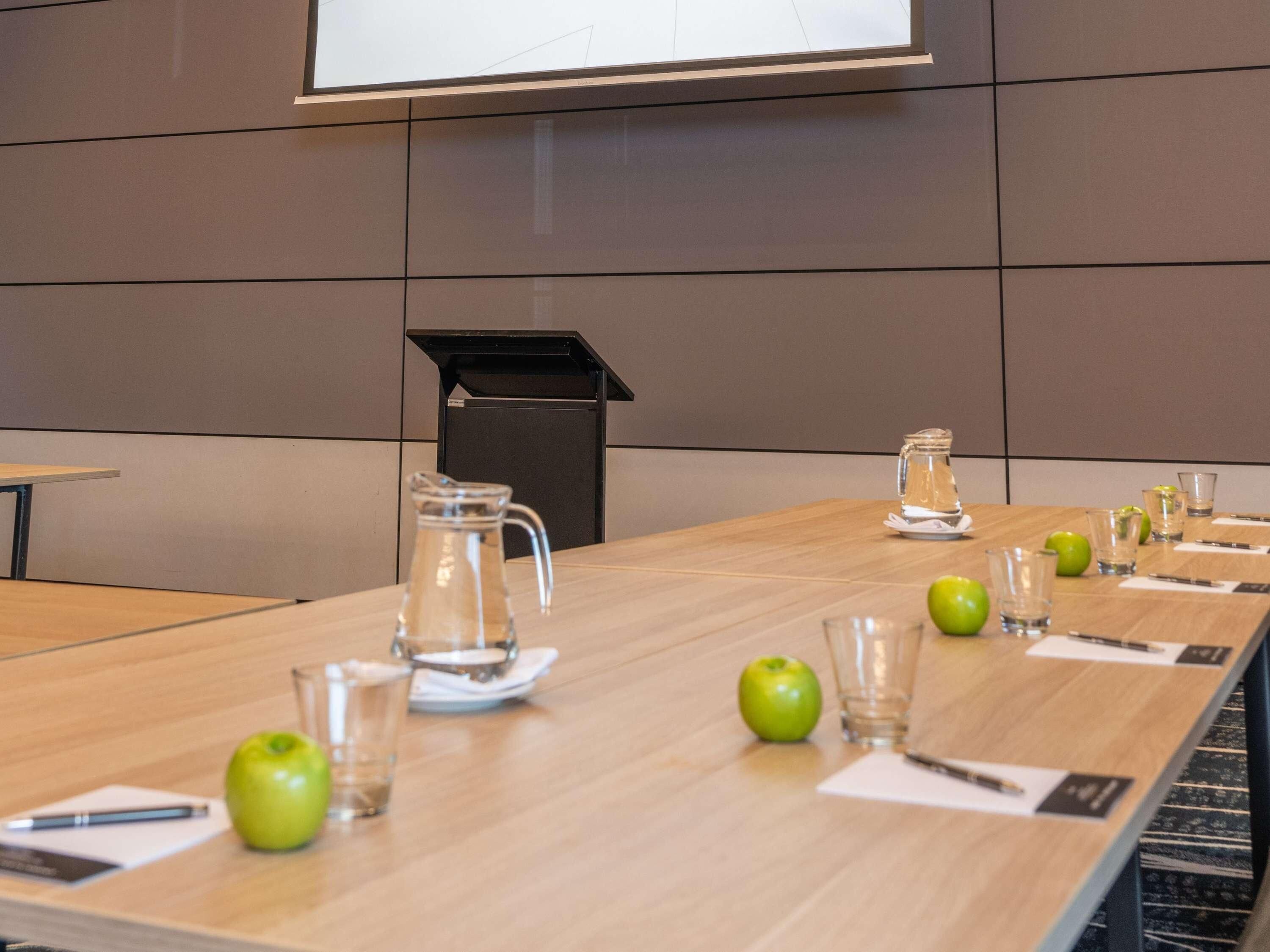 Una sala de conferencias con una mesa larga, una pantalla de proyector y un cubo de basura.
