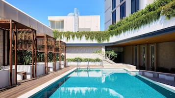 A rooftop swimming pool with a wooden deck, a stone wall, and a building with a modern design in the background.