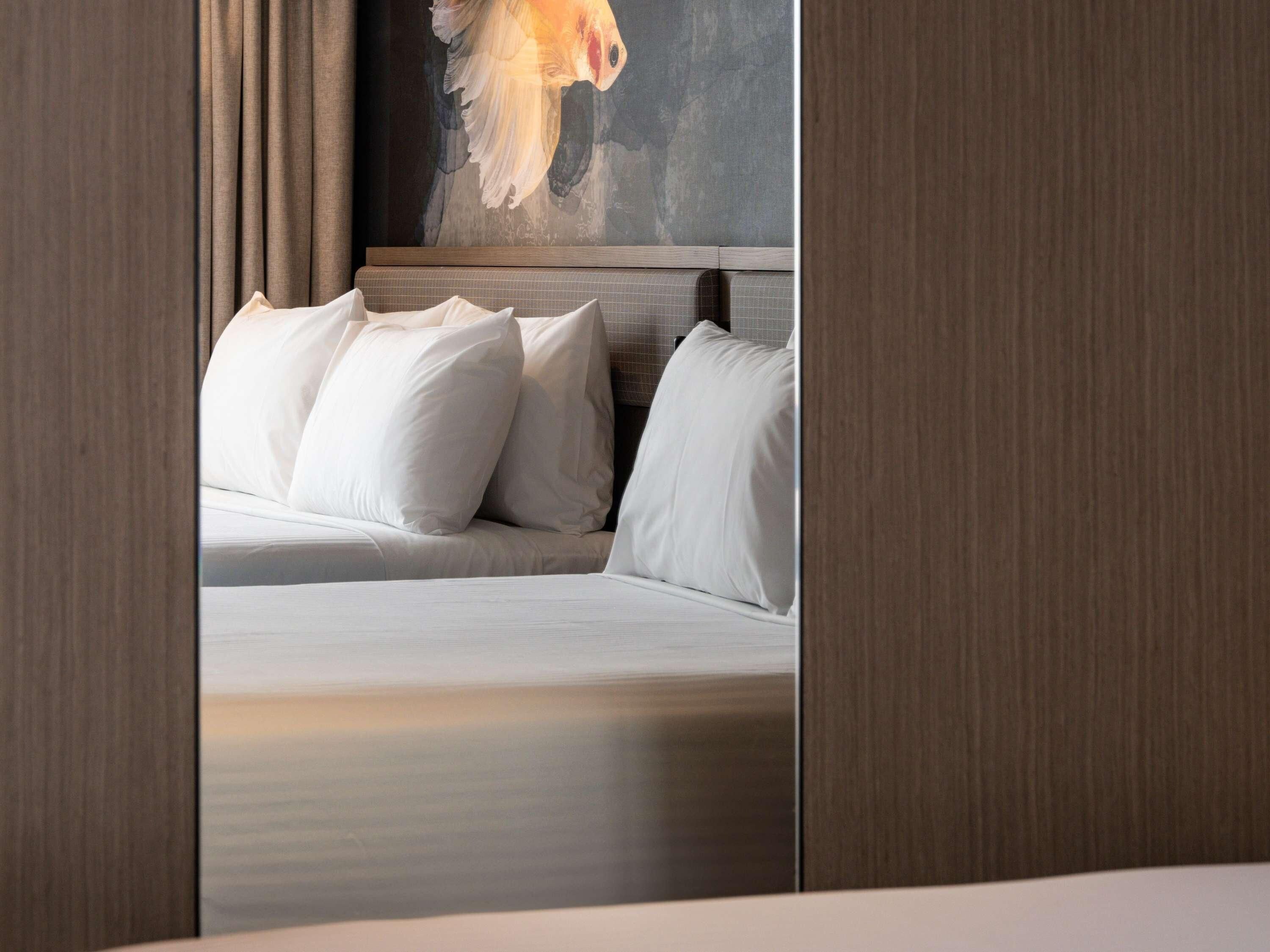 A hotel room with a bed, pillows, a painting on the wall, and wooden paneling.