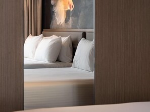 Een hotelkamer met een bed, kussens, een schilderij aan de muur en houten lambrisering.