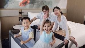 A family in a hotel room with a bed, a round table, and a wall with a fish painting. - Novotel Sydney Cabramatta (Sydney)