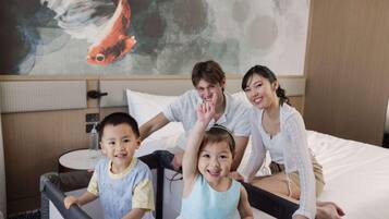 A family in a hotel room with a bed, a round table, and a wall with a fish painting.