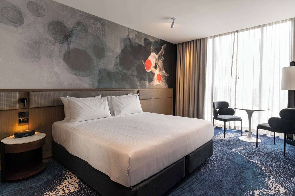 A hotel room with a large bed, a desk, a chair, and a wall with abstract art.