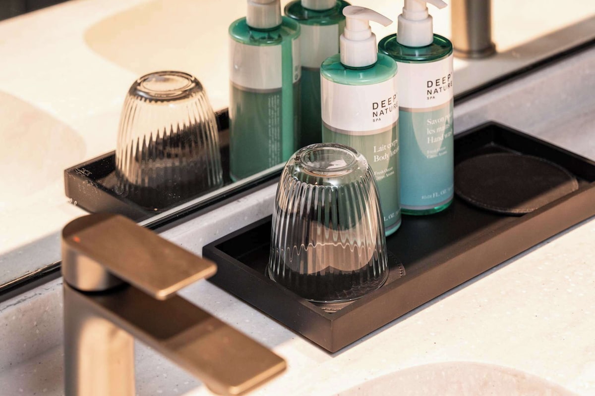 A bathroom counter with a tray holding a glass, a bottle of green liquid soap, and a bottle of lotion.