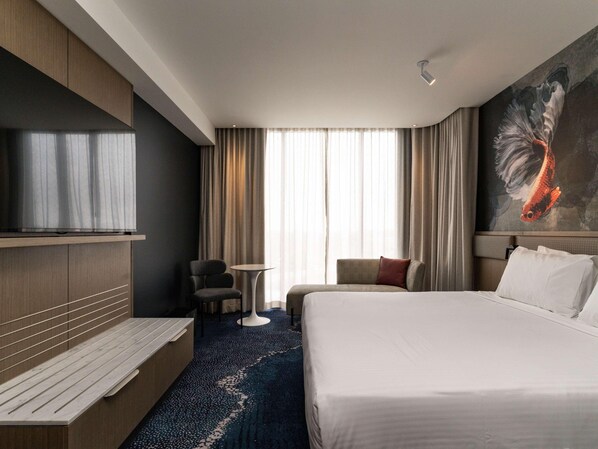 Una habitación de hotel con cama, televisión, escritorio, silla, una mesita pequeña y un cuadro en la pared.