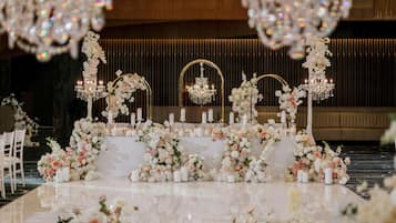 Une salle de réception de mariage aménagée avec une longue table décorée de compositions florales et de bougies, entourée de chaises.