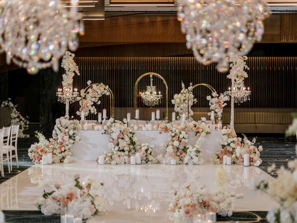 A wedding reception setup with a long table adorned with floral arrangements and candles, surrounded by chairs.