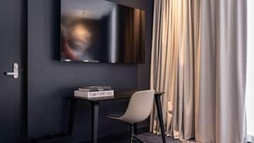 Una habitación de hotel moderna con un televisor de pantalla plana montado en la pared, una mesita con una silla y una ventana con cortinas.