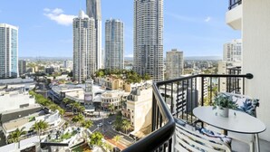 Un balcon offrant une vue sur le paysage urbain, avec de grands immeubles et des palmiers.