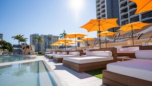 Un espace aménagé au bord de la piscine, avec des chaises longues et des parasols orange, un ciel dégagé et un bâtiment sur lequel on peut lire l’inscription « Columbia ».