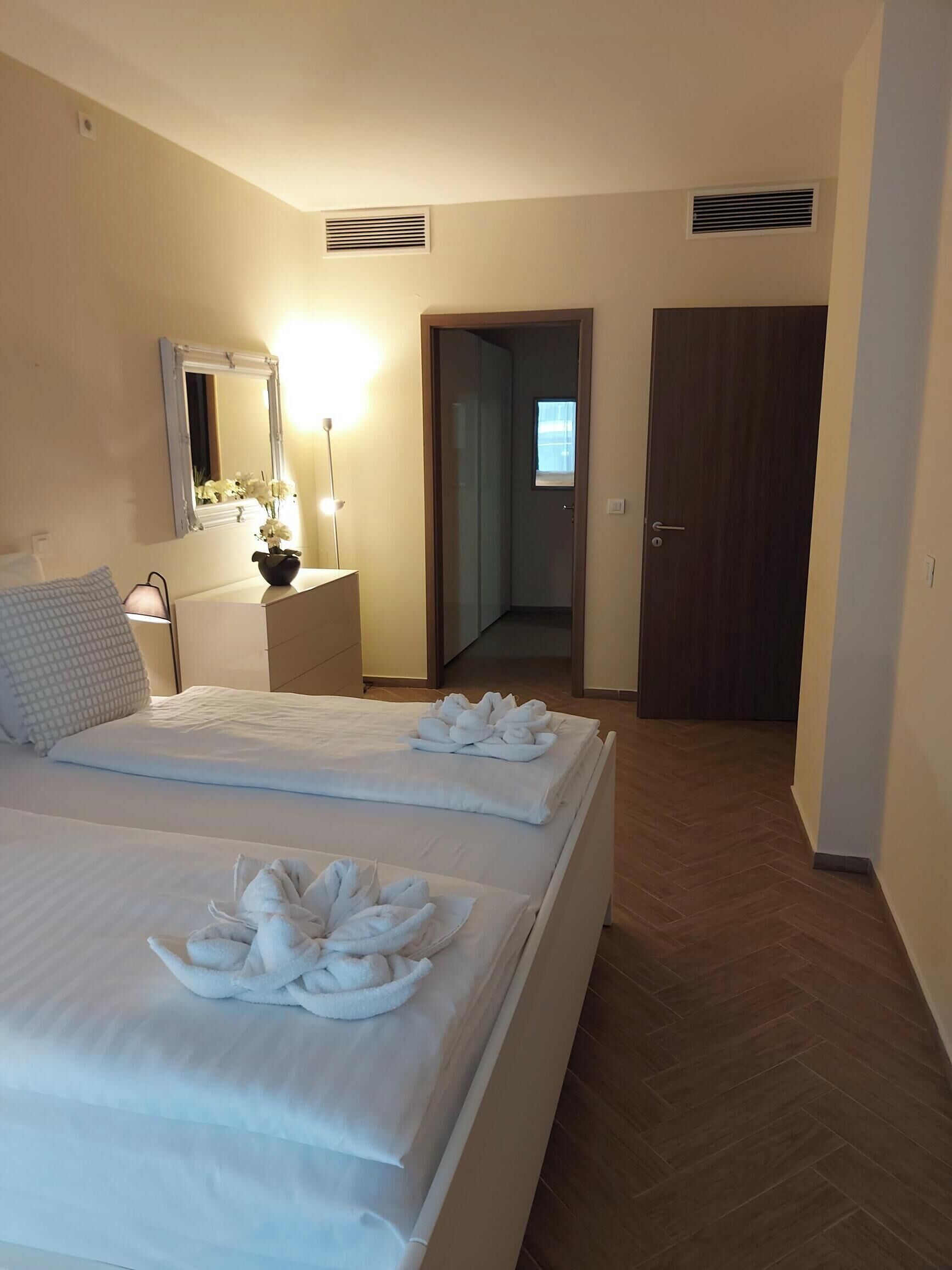 Ein Hotelzimmer mit zwei Betten, einem Nachttisch mit Lampe, einem Spiegel und einer Tür zu einem Flur.