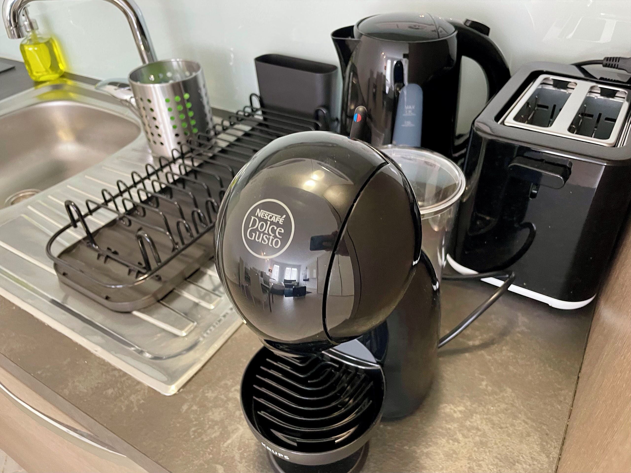 A kitchen with a coffee machine, a toaster, a kettle, and a dish rack.