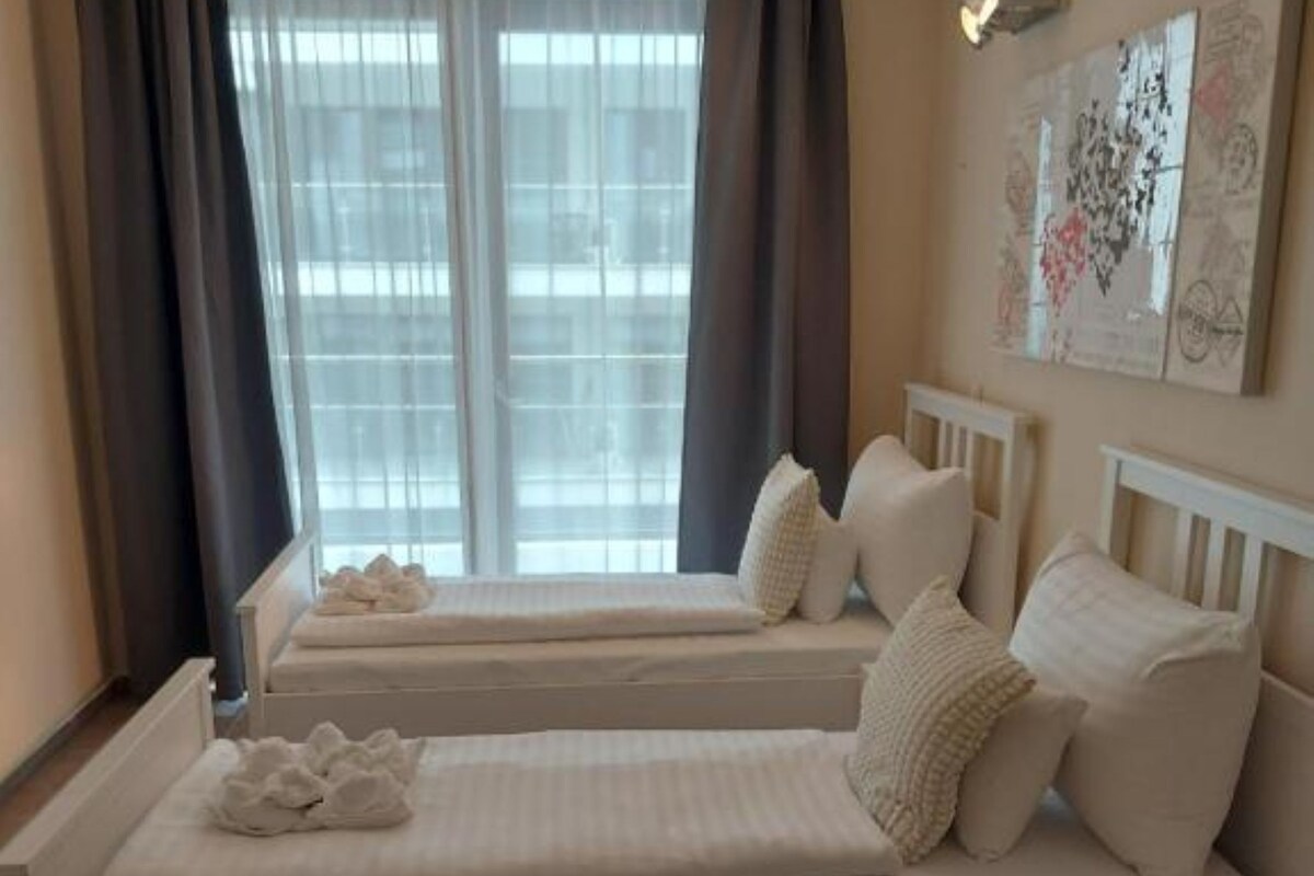 A bedroom with two beds, a window with curtains, and a wall with artwork.