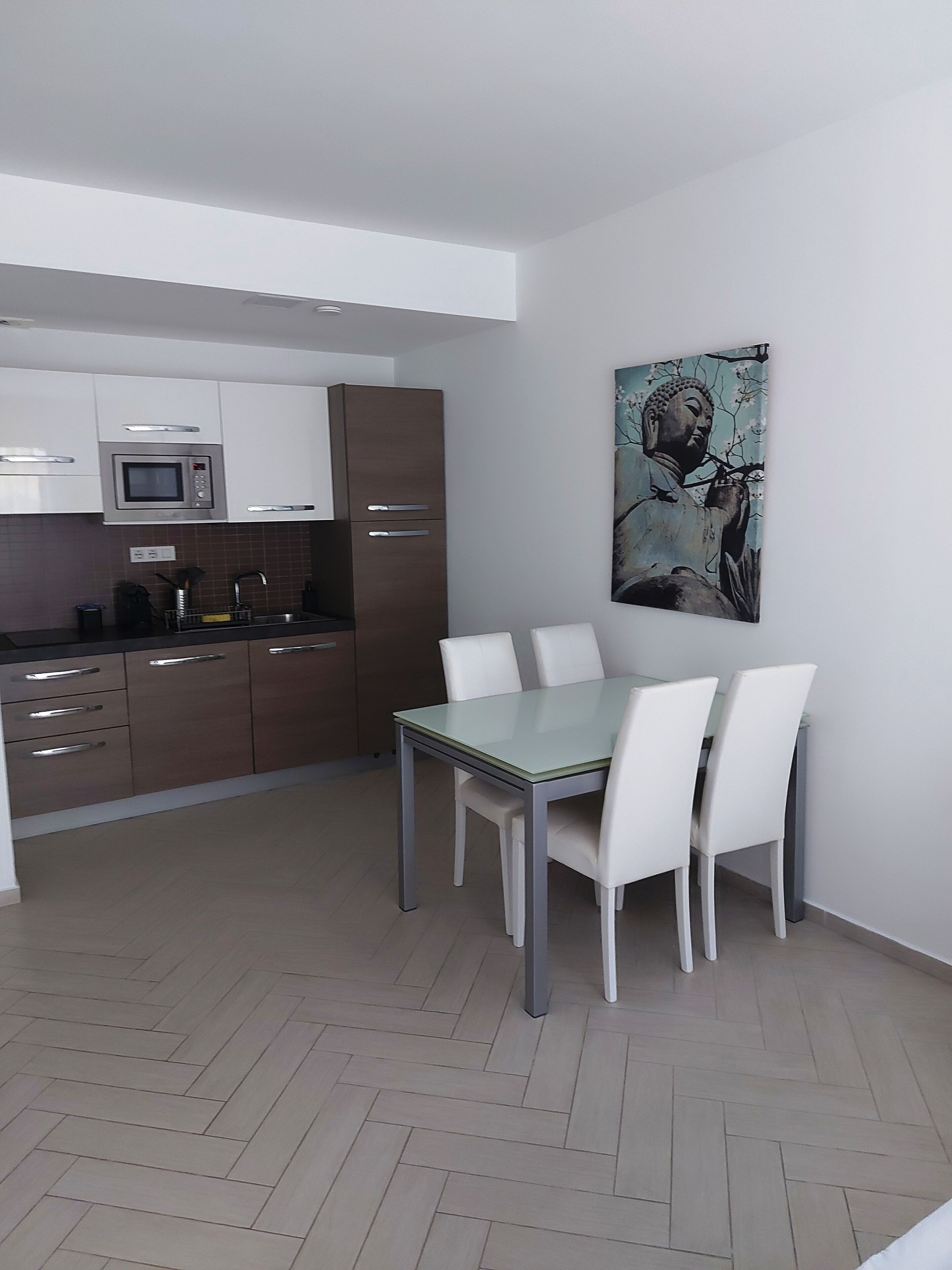 A modern kitchen with white cabinets, a microwave, and a dining area with a glass table and white chairs.