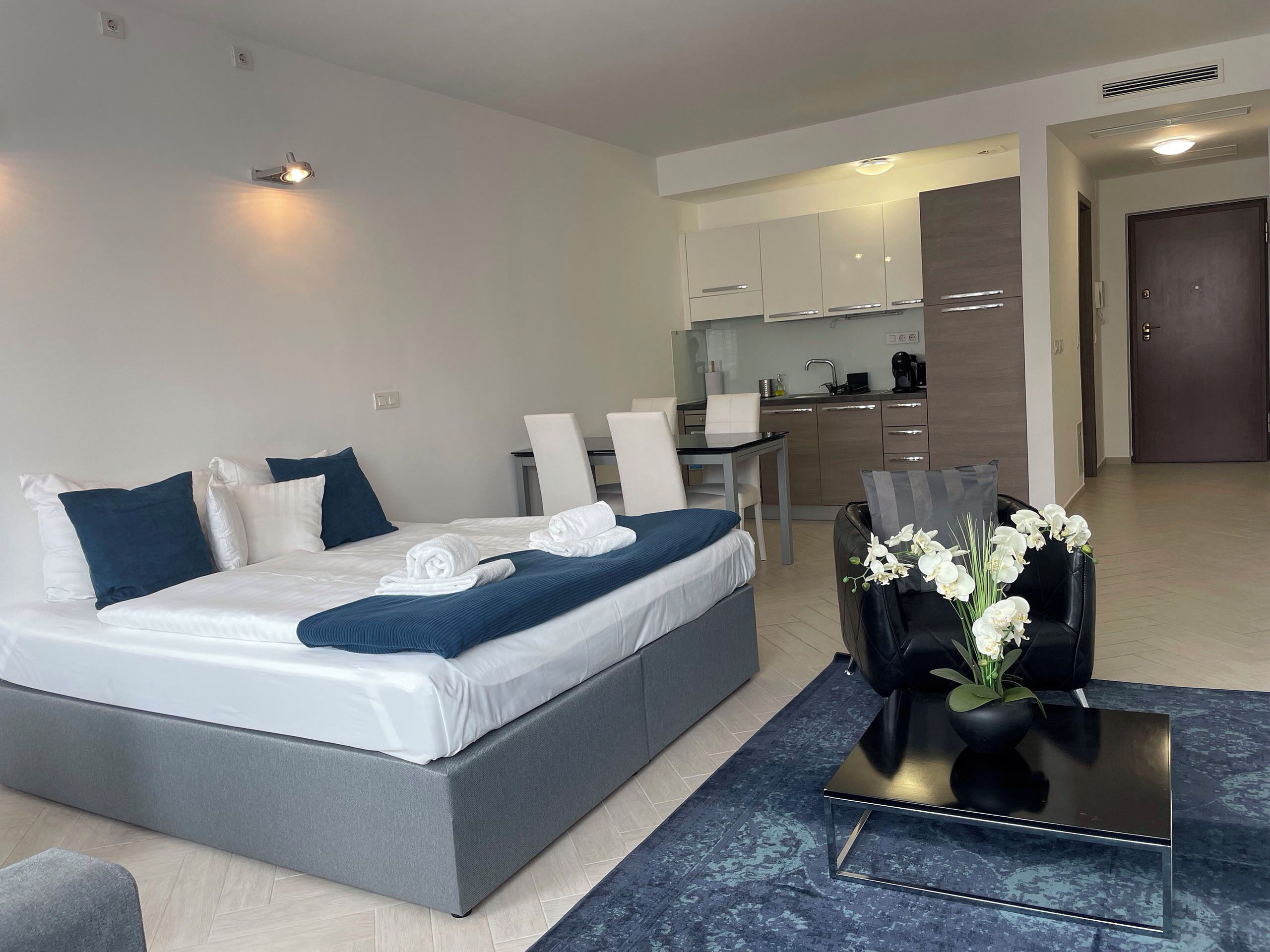 Ein modernes Hotelzimmer mit einem großen Bett, einem kleinen Esstisch, einer Couch und einer Küchenzeile.