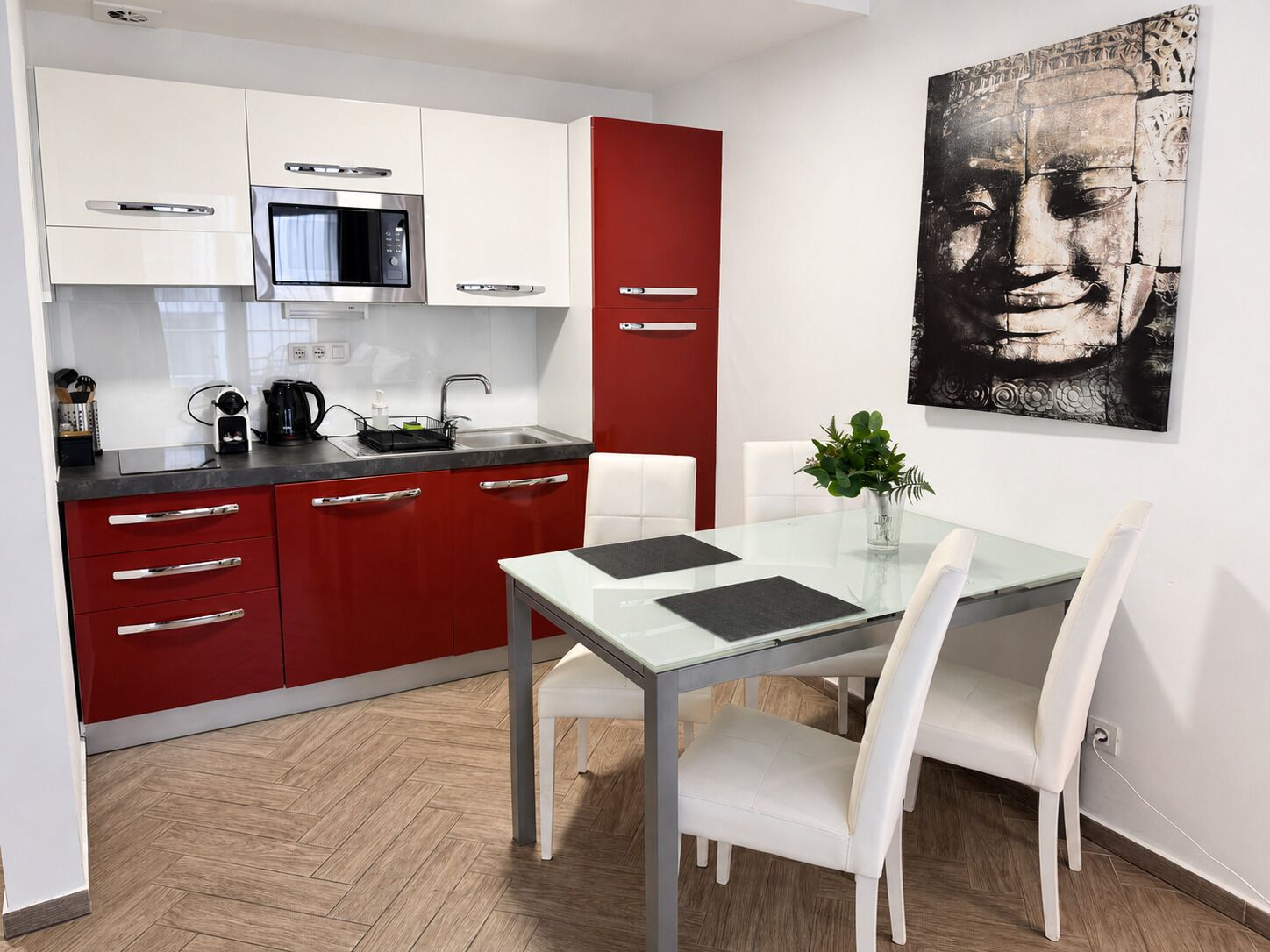 A modern kitchen with white and red cabinetry, a microwave, and a dining area with a glass table and white chairs.