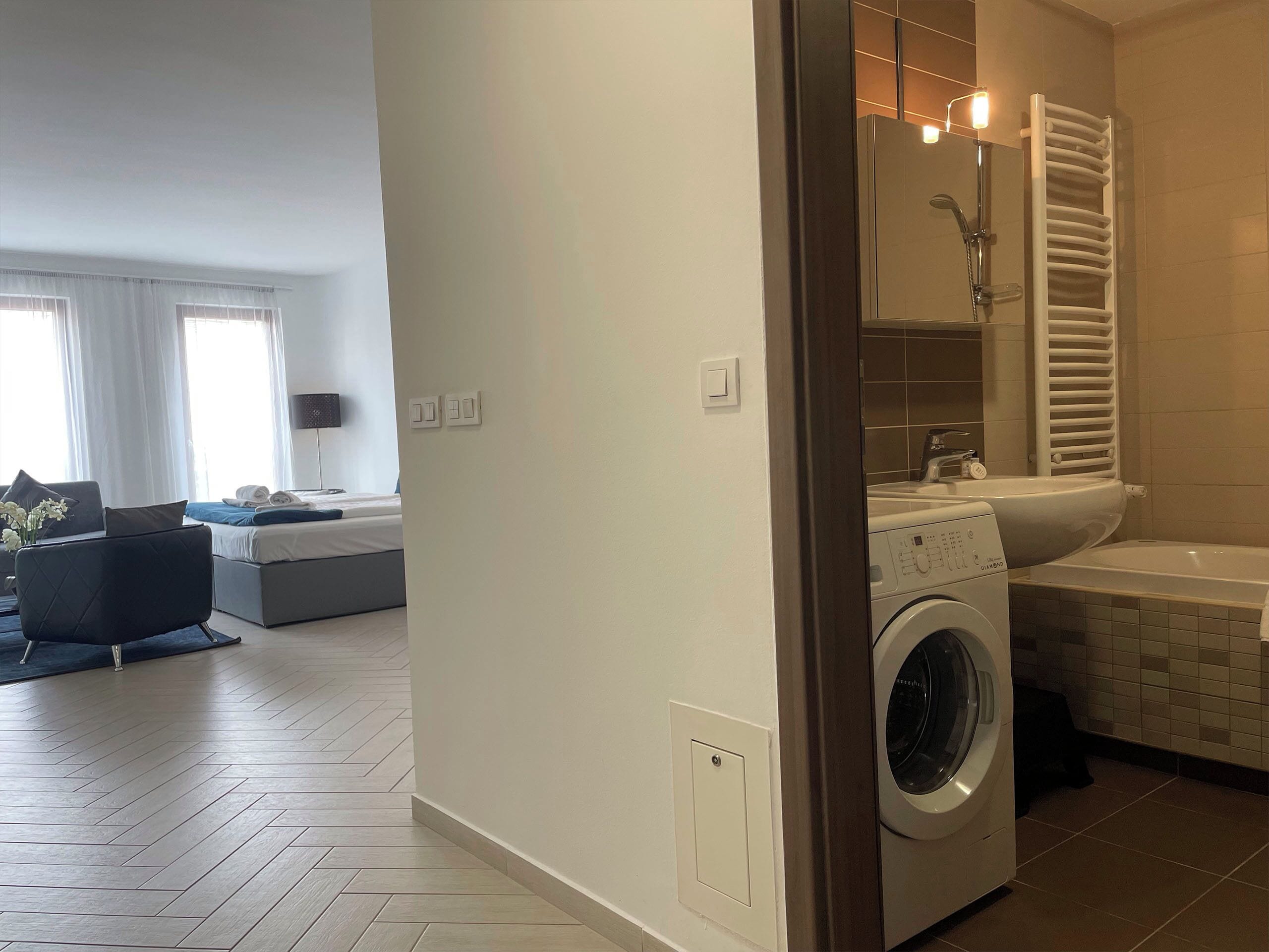 A modern apartment with a living area, a washing machine, and a bathroom with a bathtub and towel rack.