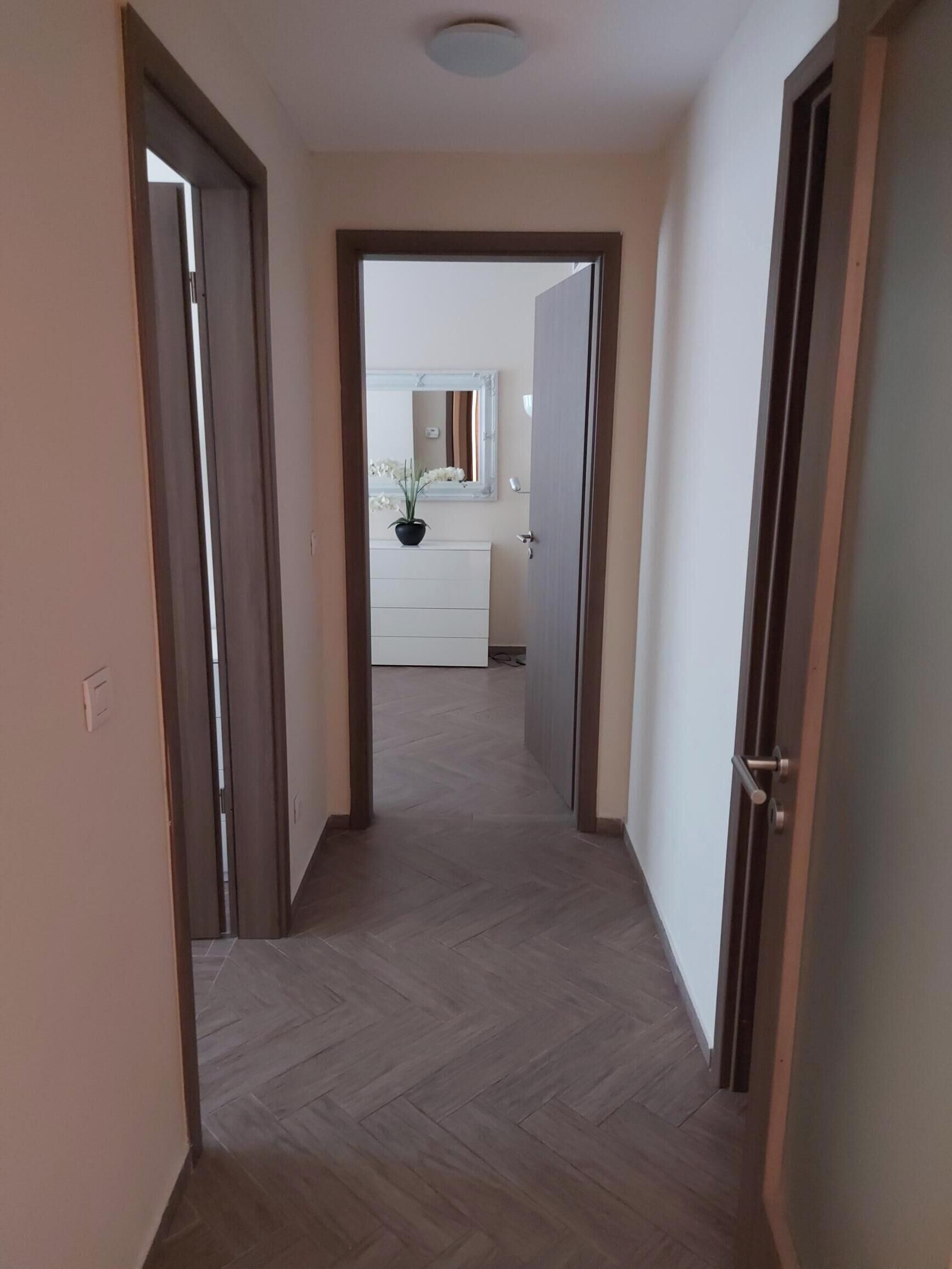 A hallway with wooden flooring leading to a bathroom with a white sink and a mirror.