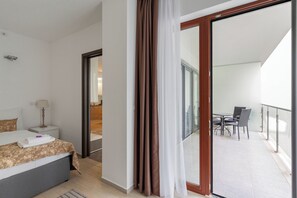 A hotel room with a bed, bedside table, lamp, and a view of a balcony with chairs. - SWU Carrara Apartments (Budapest)