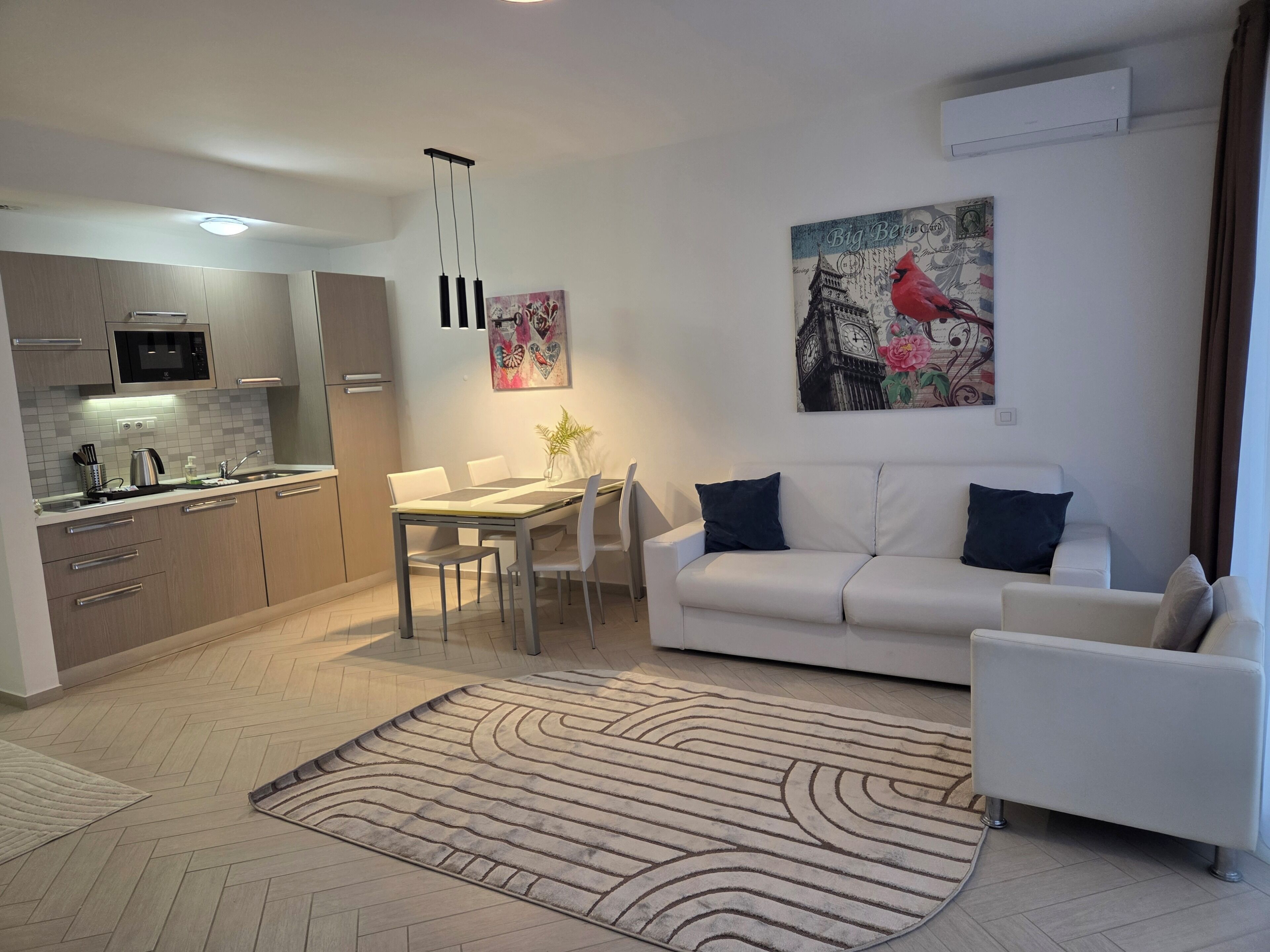 A modern living space with a dining area, white sofa, and a kitchen with a microwave.