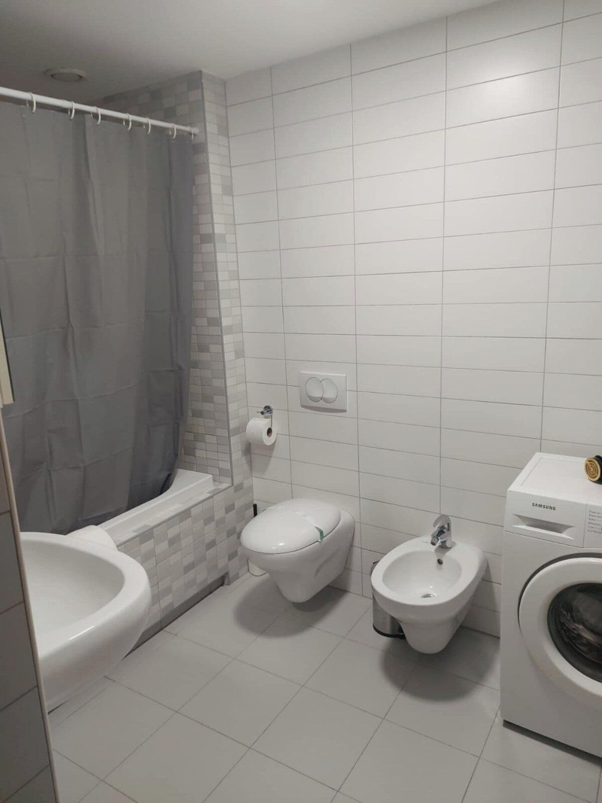 A bathroom with a bathtub, toilet, bidet, and washing machine.