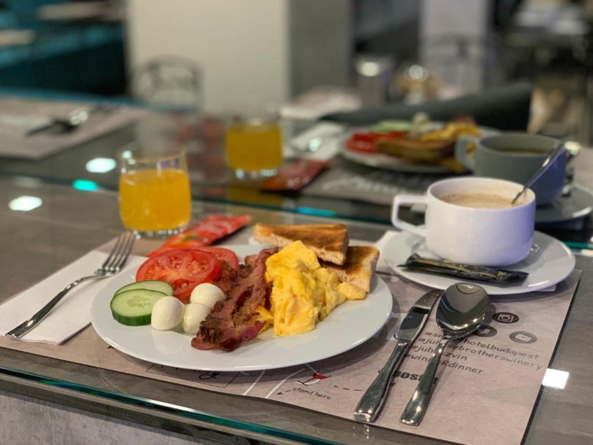 Une table mise pour le petit-déjeuner avec des toasts, des œufs, du bacon, des tomates et une tasse de café.