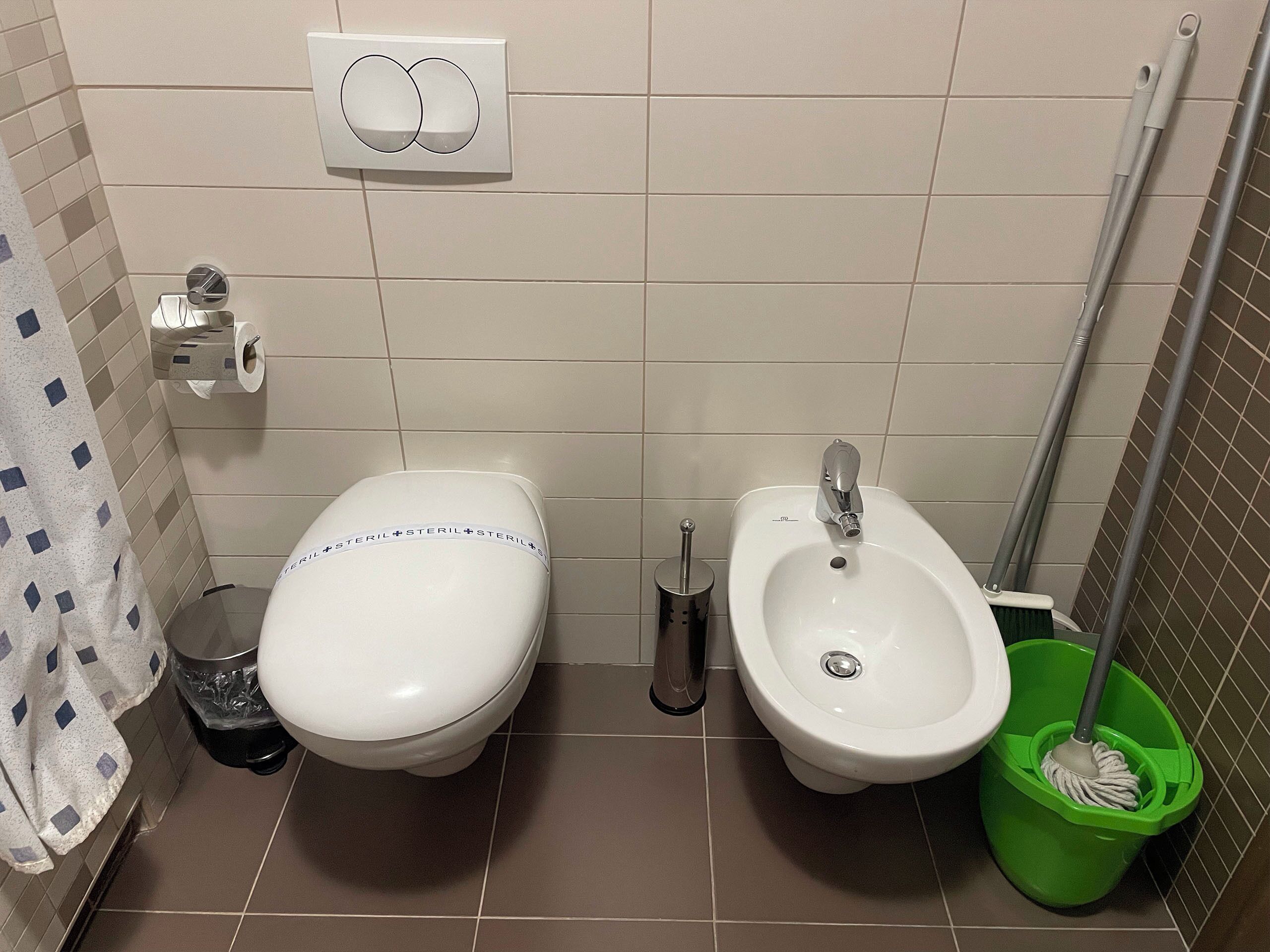 A bathroom with a toilet, bidet, and a mop.