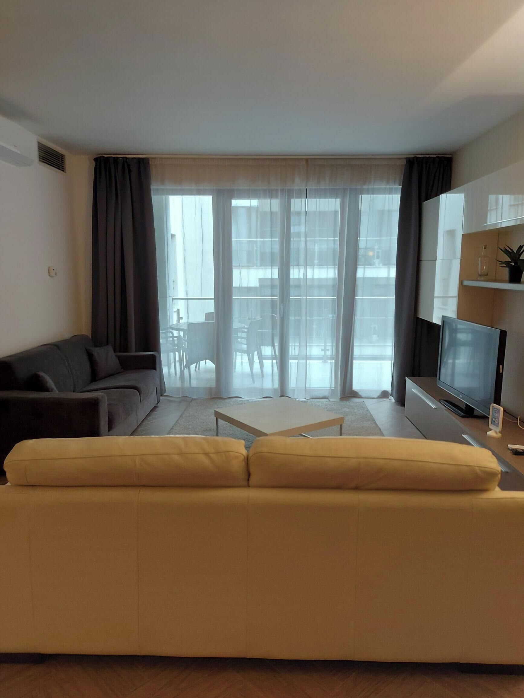 A living room with a sofa, a coffee table, a TV, and a balcony with a table and chairs.