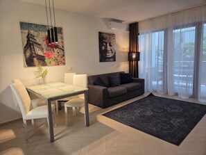 Un salon moderne avec un canapé, une table à manger et des chaises, un tapis noir et des œuvres d’art accrochées aux murs.