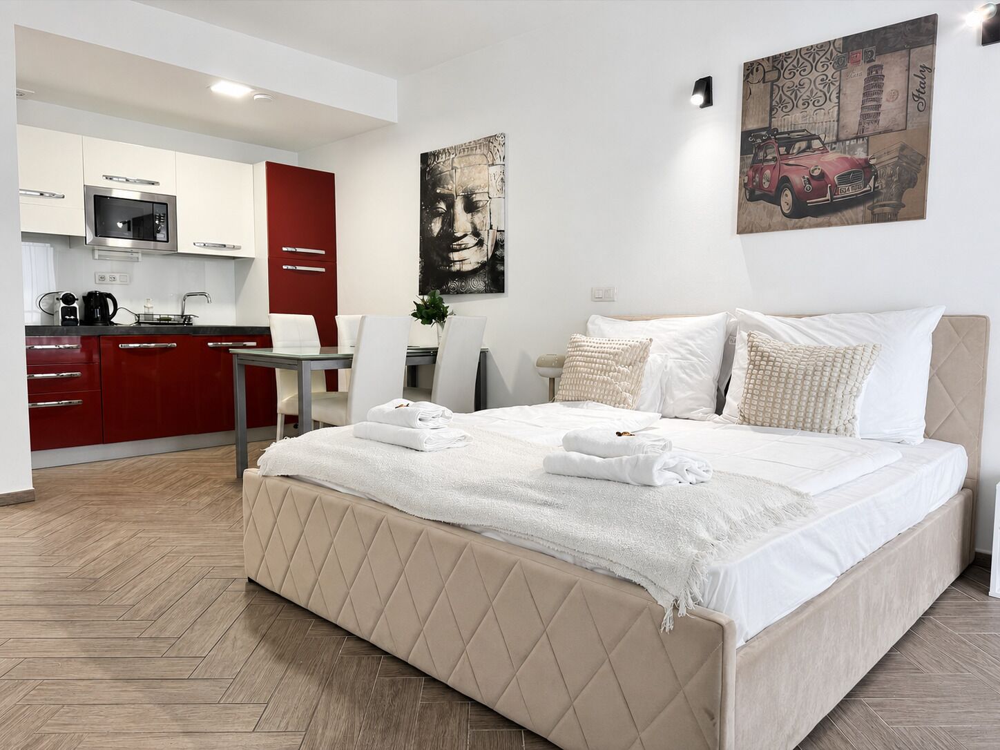 A modern hotel room with a bed, a dining area, and a kitchenette.