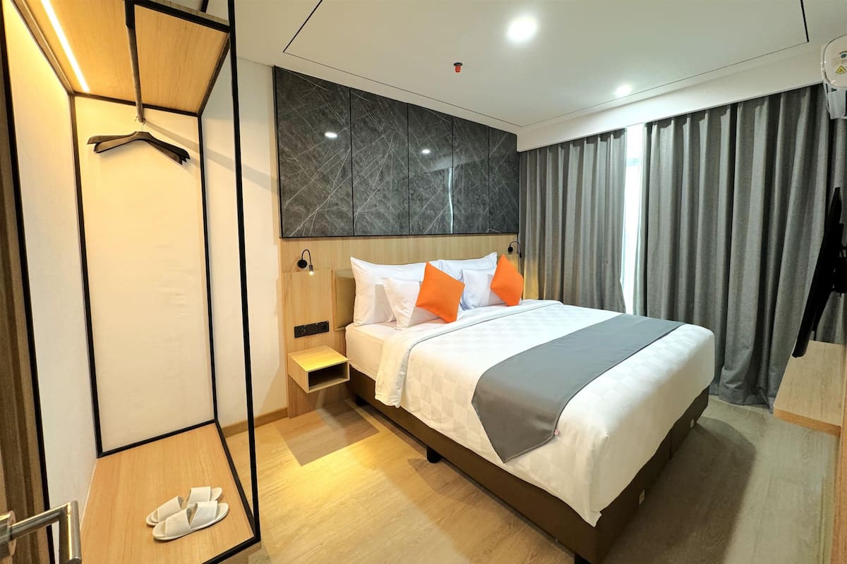 Una habitación de hotel moderna con una cama grande, una mesita de noche de madera, un pequeño rincón de descanso y un armario con espejo.