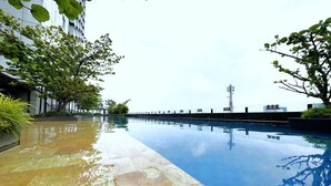 A swimming pool with a tiled deck, surrounded by greenery and modern buildings. - Howard Johnson By Wyndham Tangerang (Tangerang)
